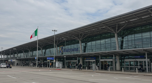Milan Malpensa Airport entrance with Italian flag and modern terminal building